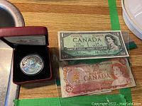 Photo of the silver coin in red display box alongside the two vintage Canadian bills in protective sleeves.