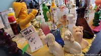 Photo showing a variety of Avon vintage collectible bottles including dog-shaped, bell-shaped, and figurine-shaped bottles arranged on a yellow cloth.