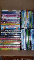 Photo showing a box of over 50 children's DVDs stacked, including titles such as Barbie, Angelina Ballerina, and All Dogs Go to Heaven.