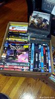 Box containing over 50 mostly sealed DVDs including Star Trek Starfleet Academy and assorted action titles.