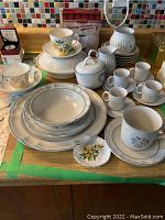 Full view of all stoneware cups, plates, bowls, sugar bowl, creamers, and small decorative plate arranged on wooden surface