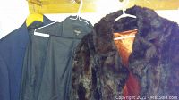 Photo showing the two jackets on hangers: a dark brown faux mink ladies jacket with plush texture and an orange lining, along with a dark suit jacket.