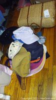 Overview of various hats and a large straw grass handbag on a wooden floor.