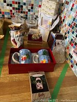 View of Staffordshire china jug, holiday mugs in red box, various ornaments including Precious Moments keepsake frames and collectible items.