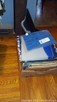 Box of assorted hanging file folders with tabbed labels, blue binder, and papers stacked on top of the box.