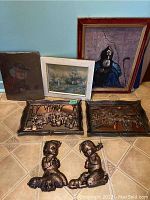 Overview photo of all lot items including 3 paintings, 4 copper finish plaques, and 2 cherub figures on a tiled floor.