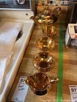 Photo showing full tea set arranged on a surface including teapot with lid, cream and sugar containers, and two cups all gold flashed.