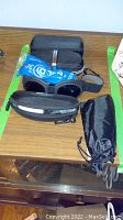 Various eyeglasses and protective cases placed on table. Includes sunglasses, magnifying glasses, sports glasses and multiple cases.