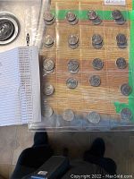 Photo showing 30 US 25-cent State commemorative quarters arranged in plastic sleeves with an accompanying checklist of states visible beside them.