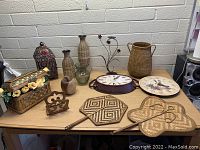 Photo of assorted home decor on table including vases, baskets, clocks, wall art, and decorative containers.