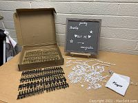 Photo showing letter sign board with gray frame and stand, black plastic letter strips in box, white plastic letters and symbols arranged on table, and white cloth pouch with Tulya branding.