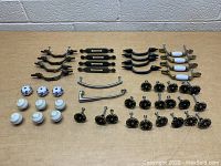 Photo showing full assortment of door and drawer pulls organized in rows on a table against a concrete block wall background
