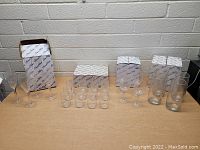 Front view of the lot arranged on table showing multiple stemmed crystal glasses, shot glasses and tumblers with original boxes behind them.
