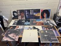 Photo showing an overall view of 22 vinyl records on a table, featuring artists such as Billy Joel, Bruce Springsteen, Richard Marx, Corey Hart, Earth Wind & Fire, and others.