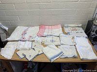 Wide view of assorted vintage linens laid out on table including embroidered and lace items