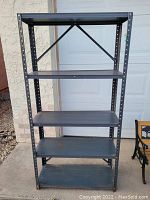 Front view of the metal shelf showing four metal shelves attached to a sturdy frame with visible wear and some rust.