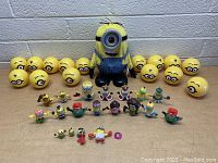 Front view of all items including the large Minion toy, expression balls, and mini figures arranged on a table in front of a wall.
