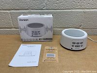 Vanzon white noise machine shown with original box, user manual, and a scratch card on a wooden surface against a brick background.
