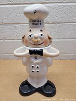 Front view of the vintage ceramic chef-shaped salt and pepper shaker set and kitchen utensil holder showing the chef's face, bow tie, and holes for salt and pepper dispensing.