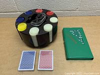 Poker chips in black rotating case alongside two decks of playing cards and a green domino set case.