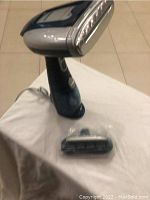 Front view of dark blue and silver Conair GS38 fabric steamer standing on white surface including separate wrapped brush attachment