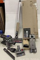 Dyson V6 vacuum with aluminum extension wand, motorized floor head, extra motorized head, charger dock, crevice tool, combination tool, and dusting brush on white surface