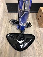Front view of blue and black steam mop with triangular mop head and power cord coiled at base.