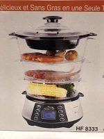Front view of the assembled food steamer with clear plastic tiers containing various vegetables and seafood. Shows digital control panel and lid.