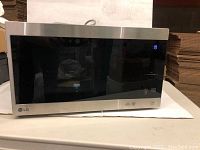 LG stainless steel microwave oven placed on a white surface, showing front with digital display and control panel