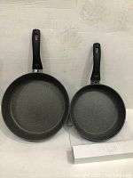 Two black frying pans with granite-style non-stick coating, 9.5 inch and 11 inch, shown side by side.