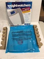 Front shot of the unopened Weightwatchers scale box alongside protective blue plastic and cardboard inserts.