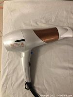 Side view of Conair hair dryer showing white body, bronze accent, and handle with power switch and tag label.