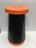 Side view of the black expandable lattice structure with orange top and bottom showing the stool expanded.