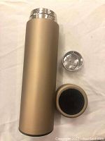 Matte gold thermal cup with digital temperature display lid and spare lid parts shown against white background.