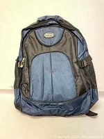 Front view of the backpack showing fabric texture, front zippered pocket, and brand logo patch.