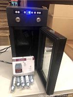 Vinotemp 2-bottle wine cooler with front glass door open, showing 5-pack unopened nitrogen cartridges placed in cooler interior.