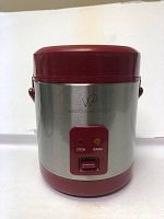 Front view of stainless steel Wolf Gang Puck rice cooker with maroon lid and base, showing cook and warm indicator lights.