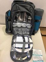 Open view of backpack showing organized cutlery, plastic glasses, and plates inside secured by straps