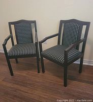 Two black wooden arm chairs with black and white polka dot fabric seat and backrest, placed on wooden floor against a beige wall.