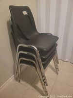 Side view of four black stacking chairs stacked together, showing plastic seat and chrome metal legs.