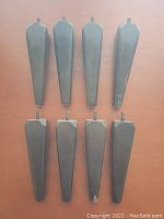 Eight wooden tapered furniture legs with dark worn finish and threaded metal inserts arranged on a wooden surface.