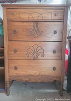 Front view of antique wooden dresser with four drawers, decorative carved wood designs, and metal ring pull handles.