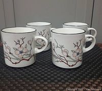 Set of four Arklow Honey Stone mugs showing pink blossom and rust branch decoration with black rim on white stoneware.