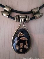 Close-up of the pendant showing black and gold pattern with silver-toned bail holding the teardrop shape.