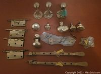 Top-down view showing an assortment of brass hinges, various door and cabinet handles, curtain rod finials, and small hardware accessories on a wooden surface.