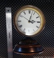 Large bronze table clock standing next to a ruler for size reference, showing about 7 inches tall.