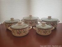 Five floral patterned cooking pots arranged with lids on, showing front designs.
