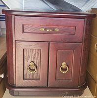 Front view of wooden night table showing drawer with brass handle and cabinet doors with brass ring pulls and visible wood grain.