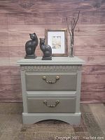 Front-facing photo of vintage night table with two drawers, showing brass handles and ornate top drawer detail.