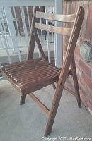 Side view of lightweight slatted wooden folding chair showing slatted seat and two horizontal slats on backrest.
